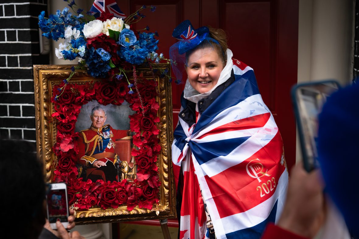 A woman in a Union Jack cape holds up a framed photo of King Charles III.