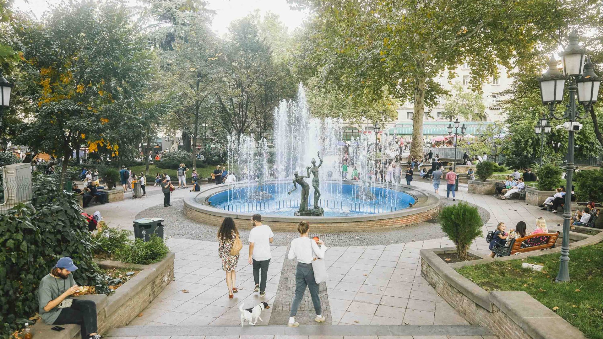 People walk through a park with a fountain.