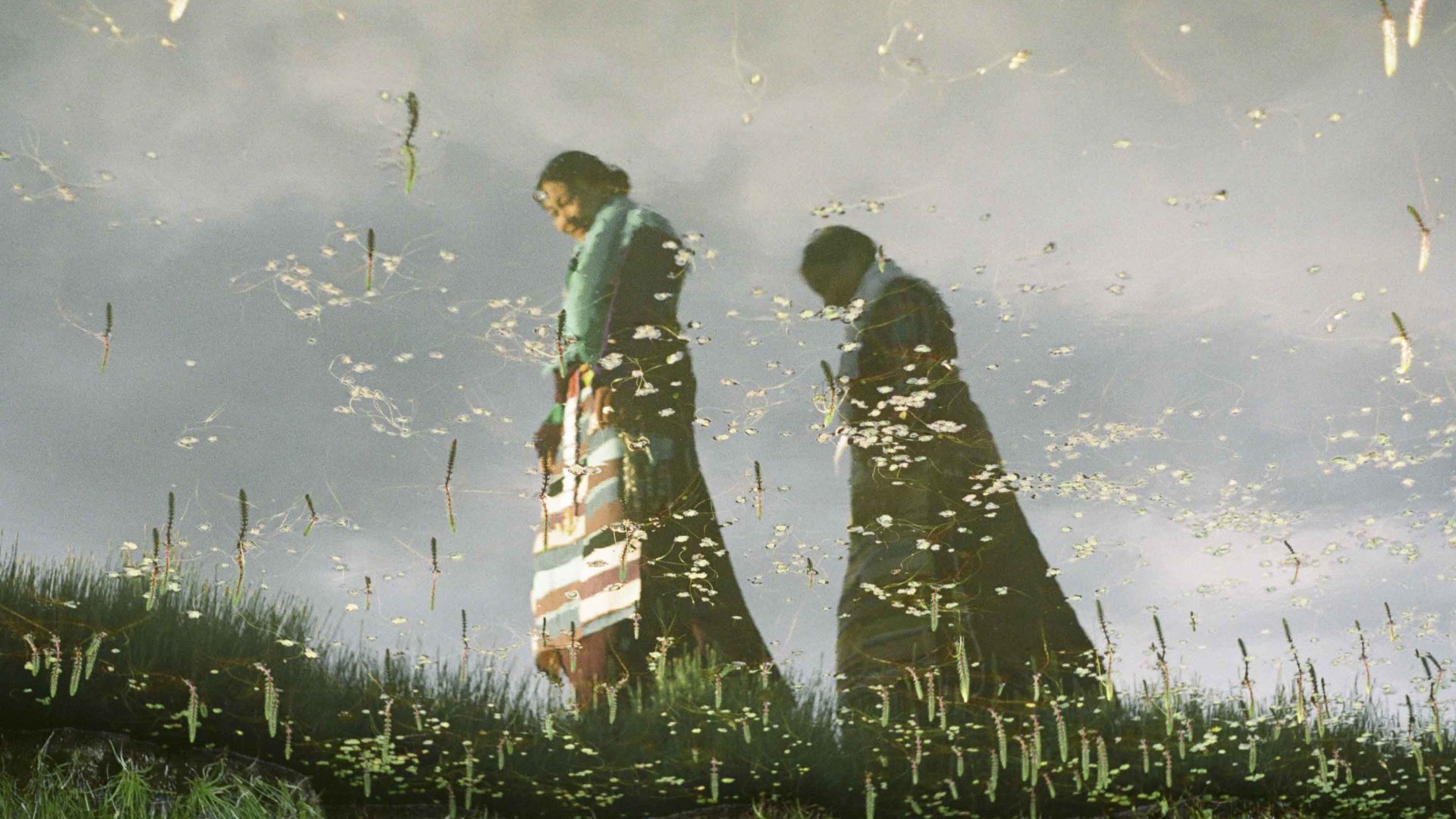 Two women in traditional textiles walk smiling through the grass.